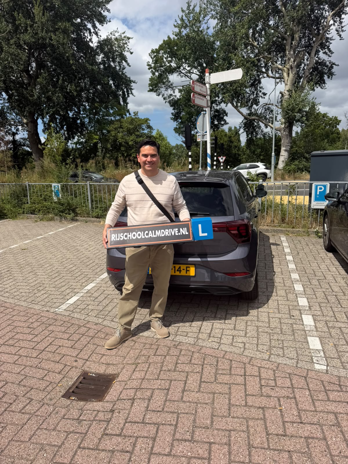 Geslaagde leerling met Calm Drive L-bord bij een grijze lesauto
